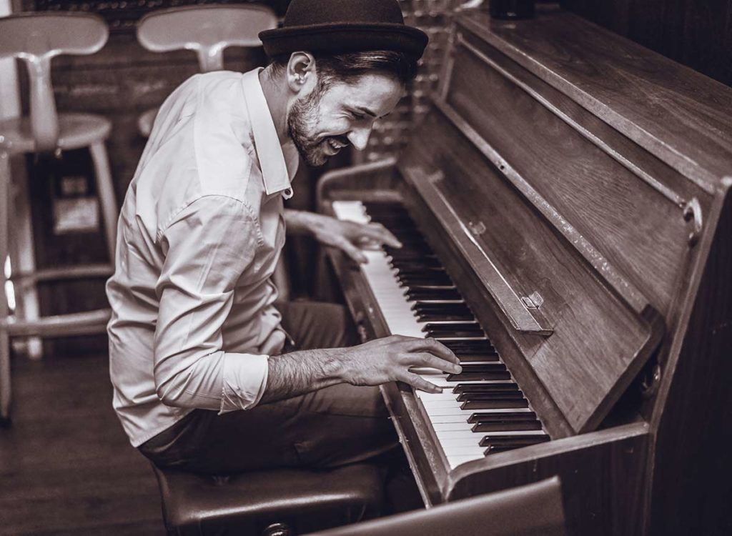 Stilig mann i skjorte og hatt spiller piano